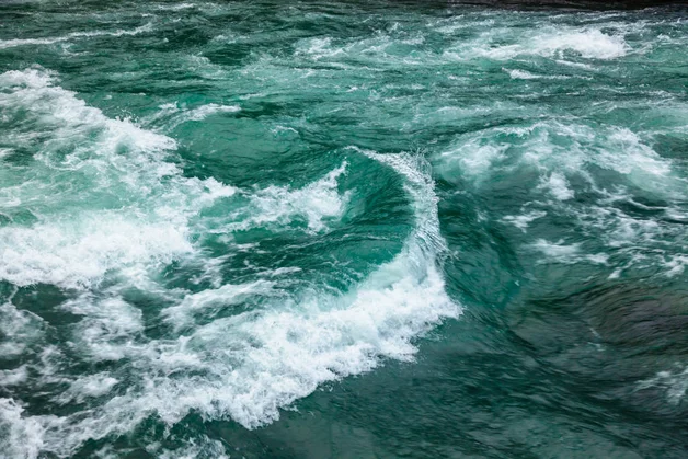 Ein dynamisches Bild von einem tiefblauen wilden schäumenden Fluss mit Strudeln.