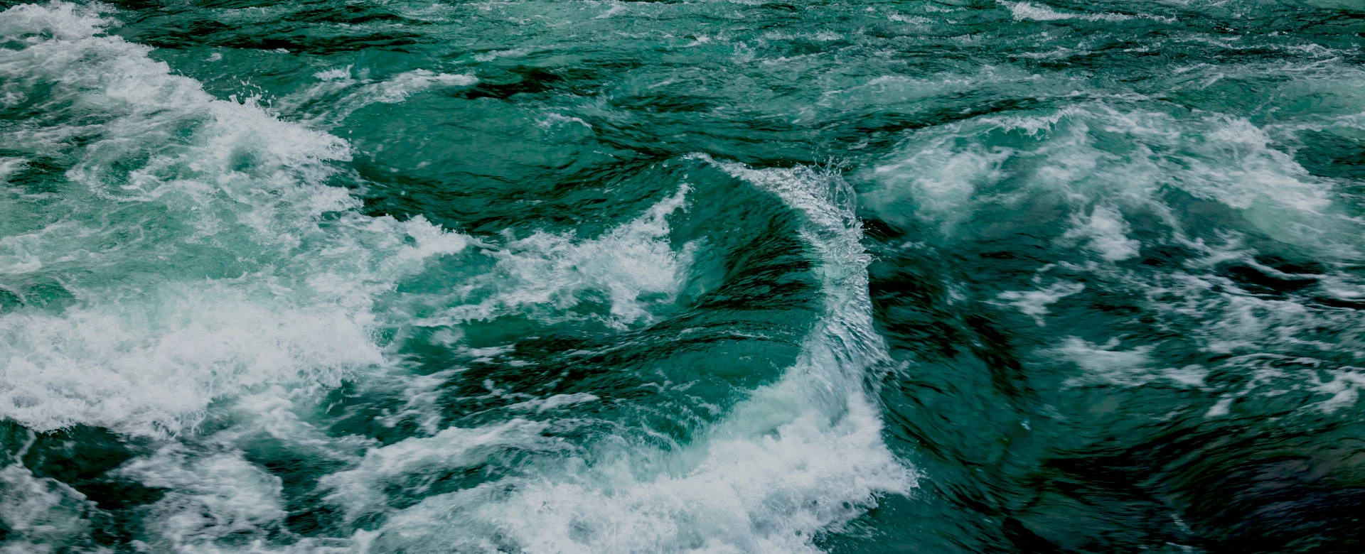 Ein dynamisches Bild von einem tiefblauen wilden schäumenden Fluss mit Strudeln.